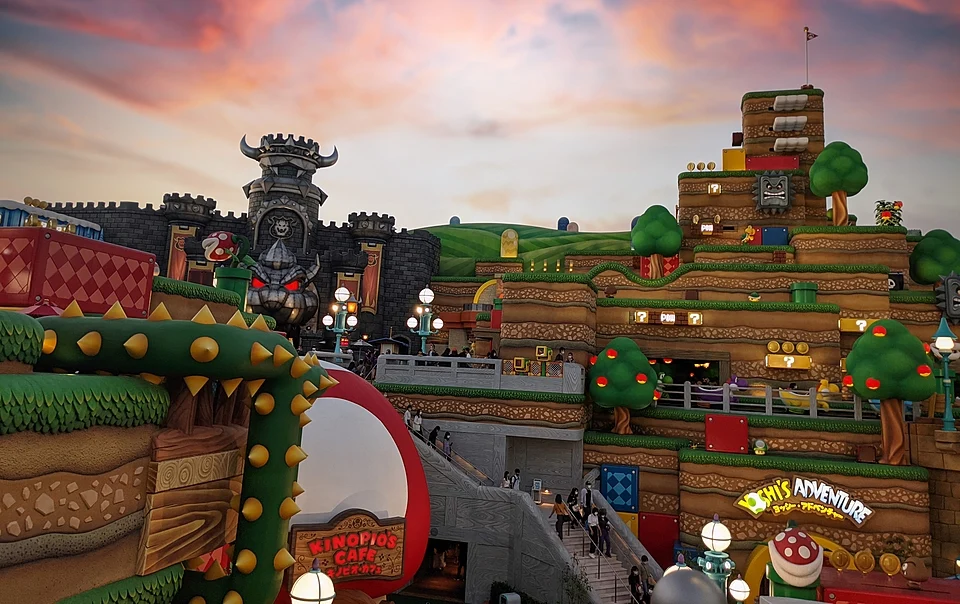 Super Nintendo World at Universal Studios Japan under a pink evening sky, with Bowser’s Castle, Kinopio’s Cafe and the Yoshi’s Adventure sign
