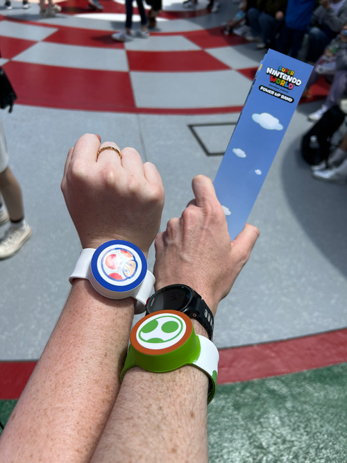 Two visitors wearing Toad and Yoshi Power-Up Bands at Super Nintendo World, Universal Studios Japan, holding the band’s blue cardboard box