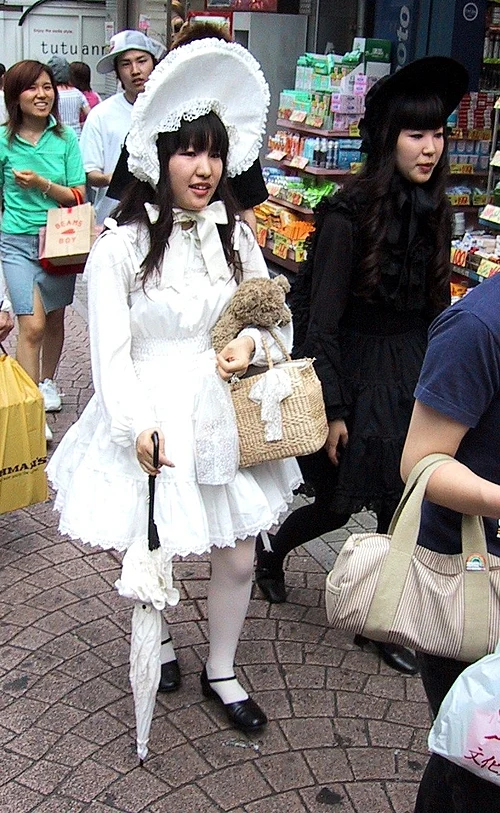 Two young women in Lolita fashion on Takeshita Street in Harajuku, one in a white sweet Lolita dress and bonnet with a parasol and the other in a black gothic Lolita outfit
