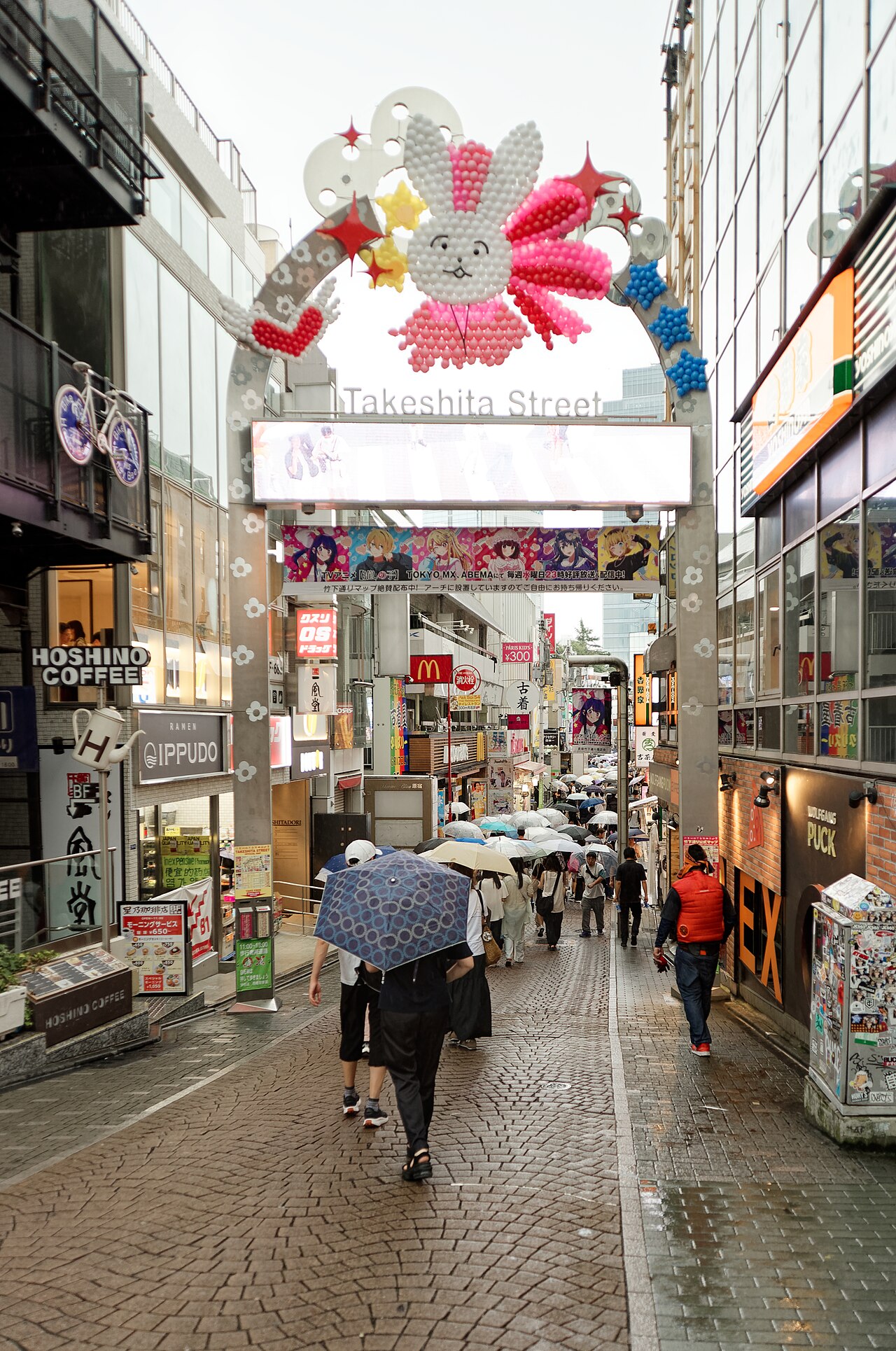 The decorated Takeshita Street entrance arch in Harajuku on a rainy day, with shops lining the narrow street