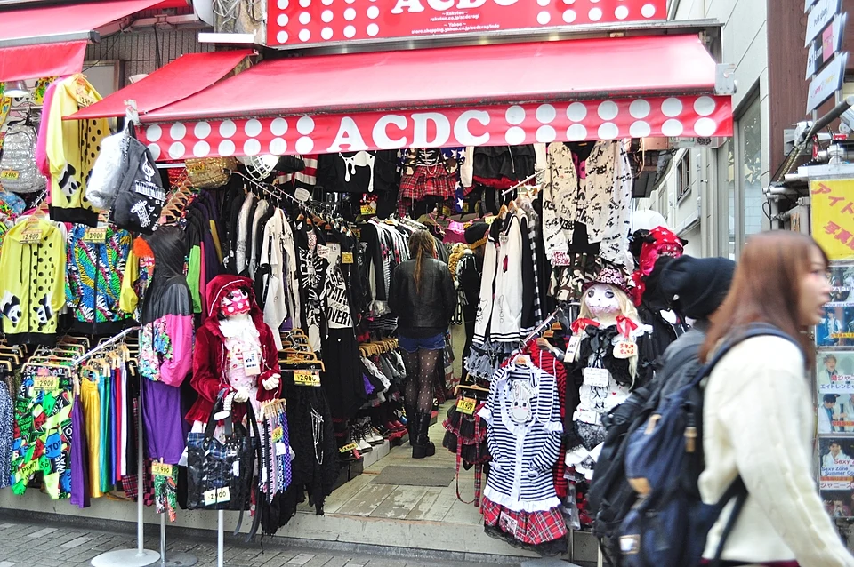 A Takeshita Street clothing shop in Harajuku with racks of colourful and gothic outfits spilling out under a red awning as shoppers browse