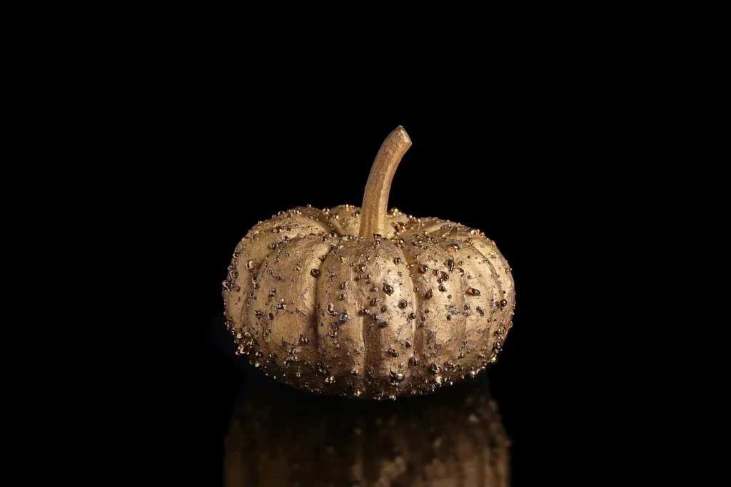 Small ceramic pumpkin in lustrous gold glaze studded with golden droplets, on a black background