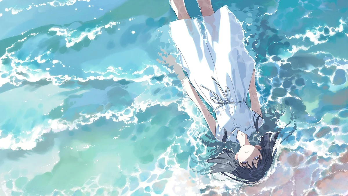 A girl in a white dress lies on her back in shallow surf, her dark hair spread across the wet sand as waves wash around her.