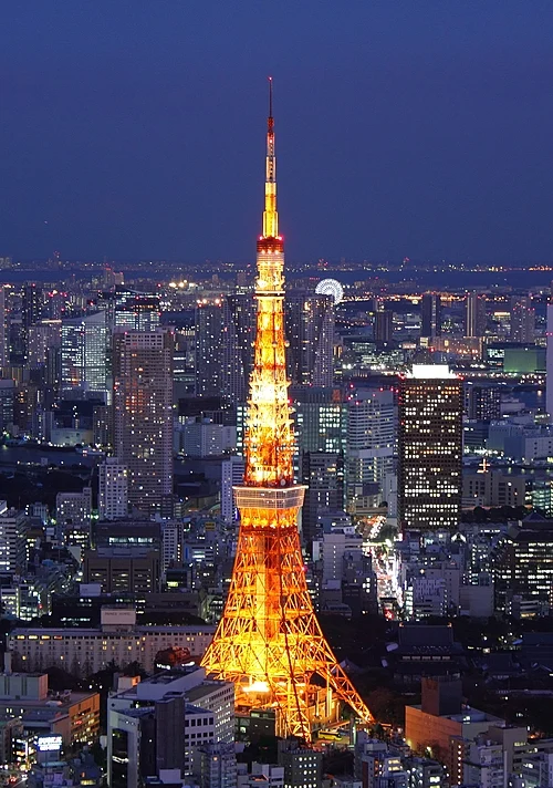 Tokyo Tower lit up in orange at night above the office blocks of central Tokyo