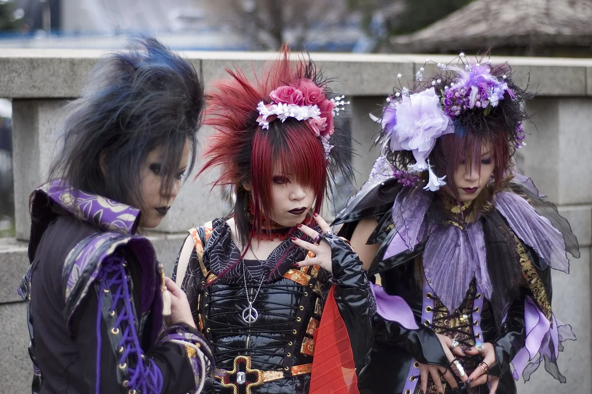 Three young people in visual kei style on Jingūbashi bridge in Harajuku, with spiked and backcombed hair in black, red and purple, black and purple costumes, lace and flower hair pieces