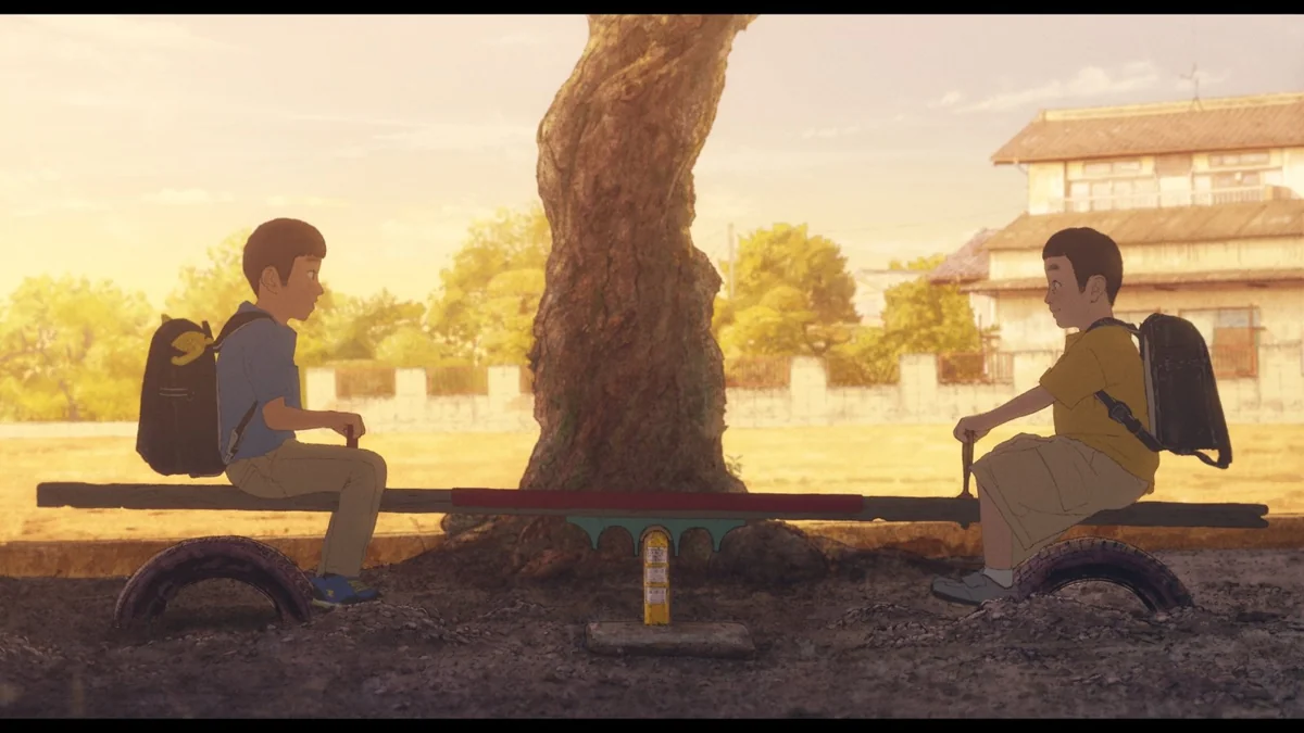 Two boys with school backpacks sit at either end of a seesaw beneath a large tree in a dusty playground, with an old wooden building behind them.