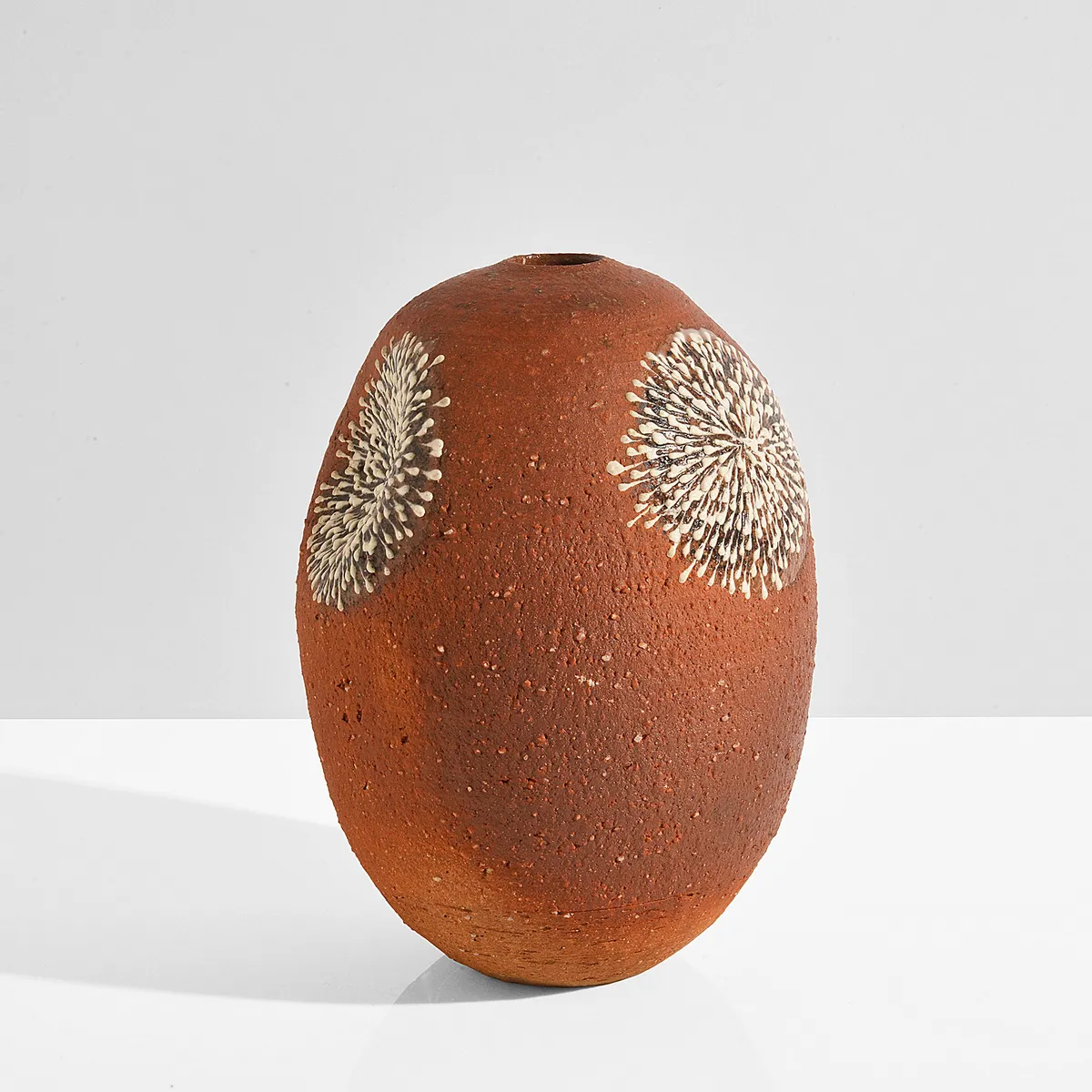 Rounded orange stoneware vase with white chrysanthemum motifs in slip, on a white surface