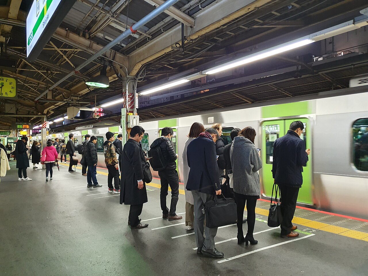 Passengers queueing in lines on the platform as a green Yamanote Line train pulls into Shinjuku Station