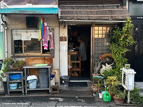 Old wooden house in Yanaka with potted plants, a watering can and household items lining the doorstep