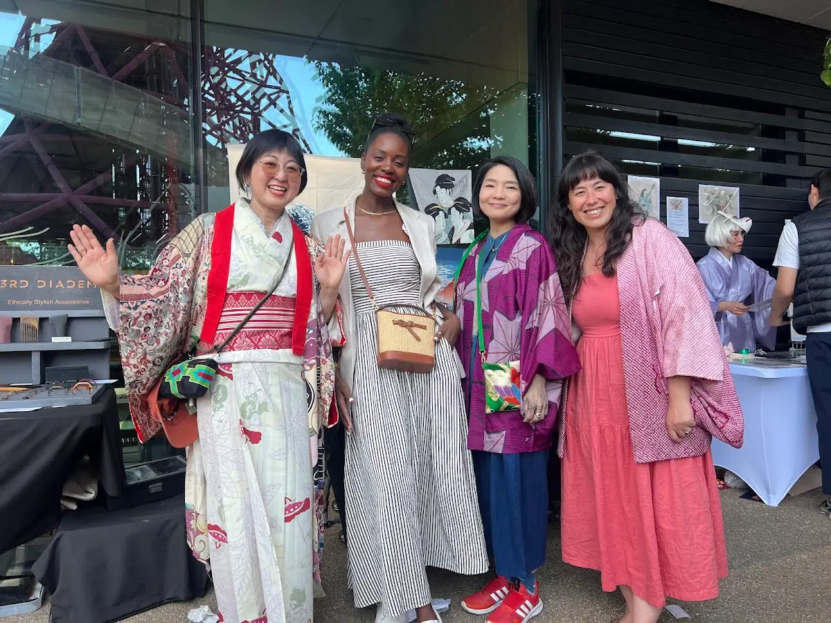 Four women, three of them in vintage kimono jackets, smiling and waving beside a stall at a Yokimono Japanese Market