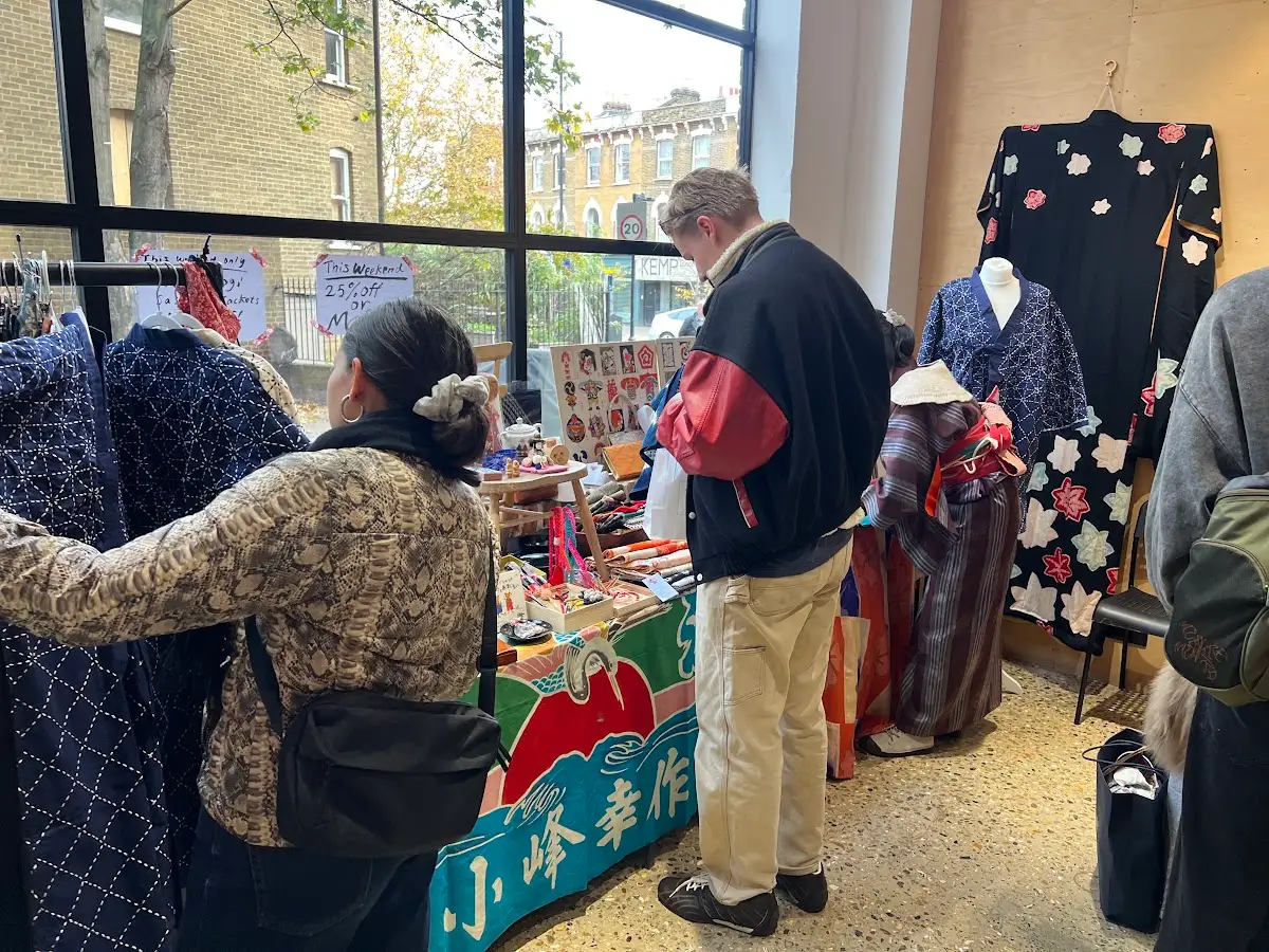 Shoppers browsing indigo jackets and kimono on mannequins at a Yokimono Japanese Market stall, with a painted Japanese banner hanging from the table
