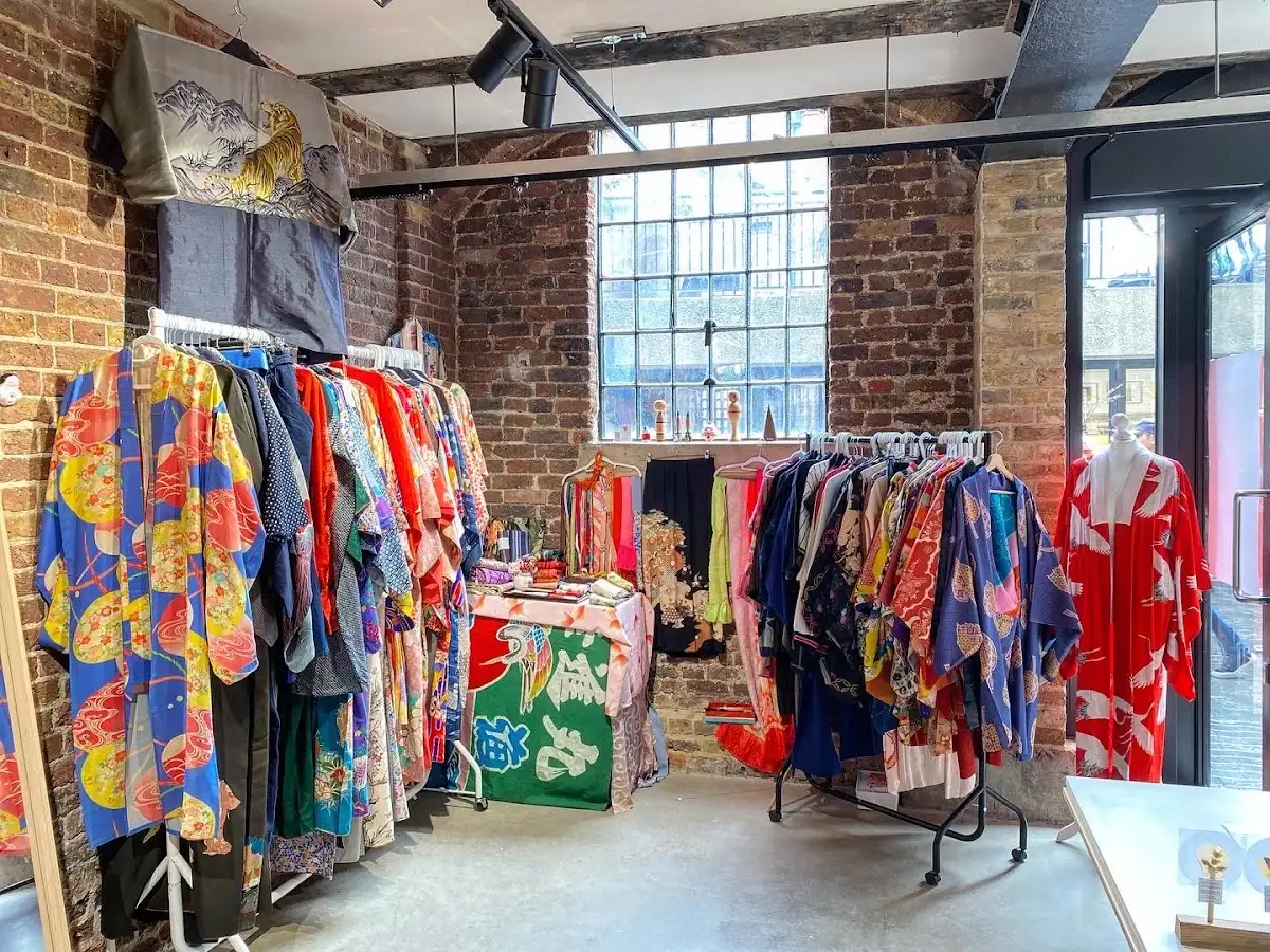 Rails of brightly patterned vintage kimono and haori in a brick-walled room with a tall factory window