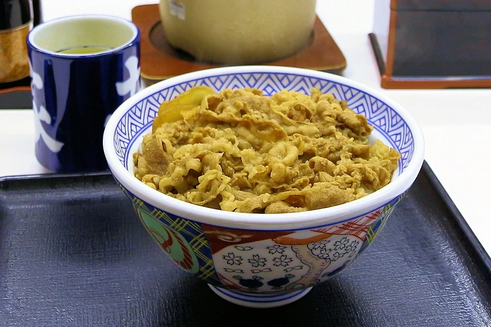 Bowl of gyudon, thin sliced beef and onion over rice, on a black tray with a cup of green tea at a Yoshinoya restaurant in Osaka